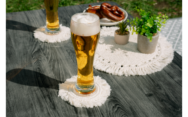 Deux verres de bière avec mousse sur des dessous de verre blancs sur une table en bois foncé, à l'arrière-plan une assiette de bretzels et deux petits pots de plantes
