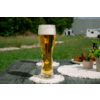 Grand verre de bière claire avec mousse sur une table à l'extérieur, sous-verre blanc, pelouse et caravane en arrière-plan