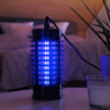 Elektronische Insektenfalle mit blau leuchtendem Licht neben einer Pflanze und einem Glas