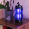 Schwarzes elektrisches Insektenvernichtungsgerät mit blauem Licht auf einem Holztisch neben einer Topfpflanze