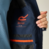 Innenansicht einer dunkelblauen Jacke; innen ein orangefarbenes Logo 'Regatta Great Outdoors' mit Text 'EST. 1985' und zwei horizontale Streifen (orange und dunkelblau) an der Innentasche; eine Hand hält die Jacke geöffnet