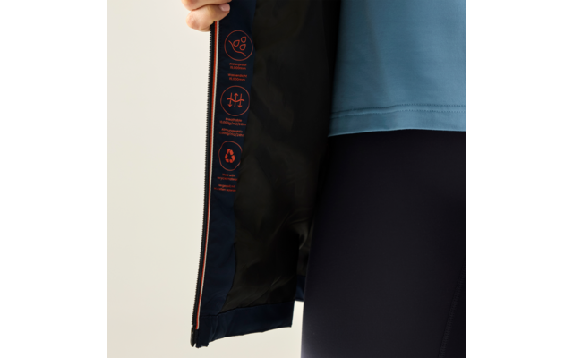 Hand hält Jacke geöffnet; dunkelblaue Innenfütterung mit drei orangefarbenen Symbolen; Person trägt hellblaues Oberteil und dunkle Leggings