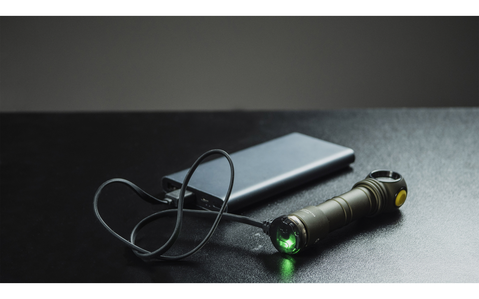 Kleine Taschenlampe mit grünem Licht, verbunden mit einer mobilen Powerbank auf dunklem Untergrund