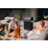 Vier Erwachsene sitzen auf Außensofas um einen niedrigen Tisch auf einer Terrasse; ein Gasgrill, Weingläser, Kissen und Pflanzen sind sichtbar