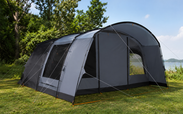 Grande tenda a tunnel grigia sull'erba, diverse finestre, ingresso aperto, tiranti, alberi sullo sfondo, acqua a destra, cielo azzurro con poche nuvole