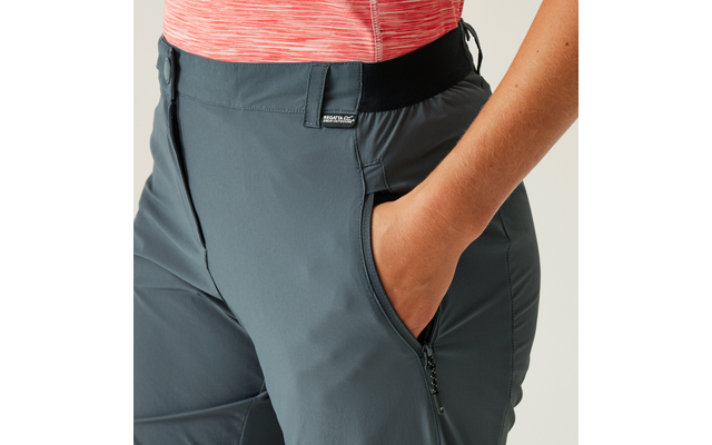 Oberkörper mit korallfarbenem Shirt und grauer Hose, rechte Hand in rechter Hosentasche