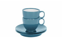 Deux tasses bleues avec anses empilées sur deux soucoupes sur fond blanc