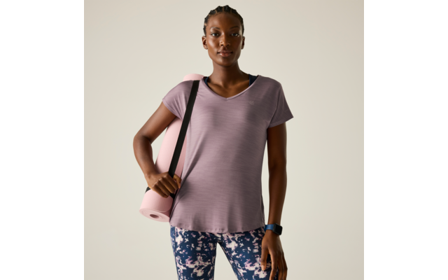 Person steht frontal, trägt violettes T‑Shirt und gemusterte Leggings, hält eine rosa Yogamatte über der Schulter; Armbanduhr am Handgelenk