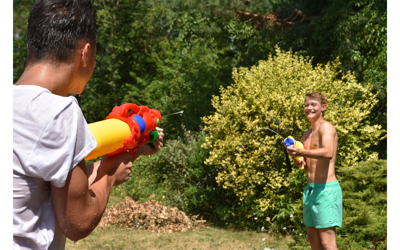 Zwei Kinder spielen mit Wasserpistolen im Garten, umgeben von Büschen