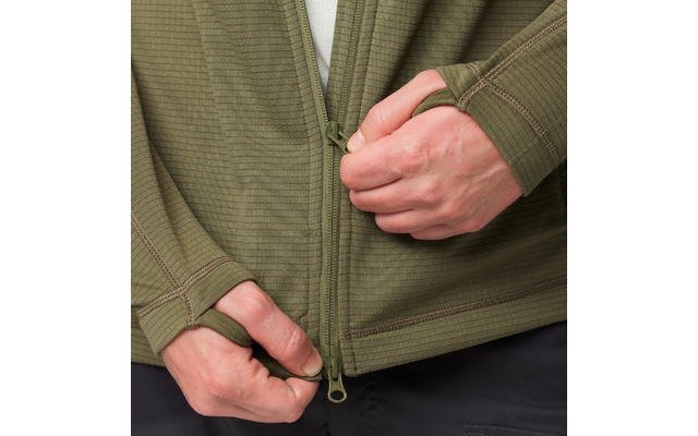 Nahaufnahme zweier Hände, die den Reißverschluss einer olivgrünen, gerippten Jacke mit Daumenlöchern hochziehen; dunkle Hose sichtbar