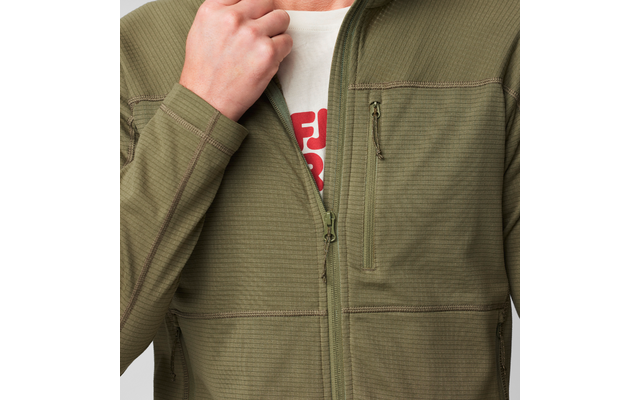 Oberkörper einer Person in olivgrüner, strukturierter Zip‑Jacke, linke Hand hält den Kragen, Jacke teilweise geöffnet, darunter weißes T‑Shirt mit rotem Schriftzug