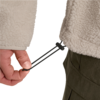 Hand hält schwarzen Kordelzug mit Stopper am Saum einer beige Fleecejacke; grüne Hose sichtbar