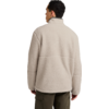 Rückansicht einer Person mit kurzem dunklem Haar, trägt eine beige Fleecejacke und olivgrüne Hosen