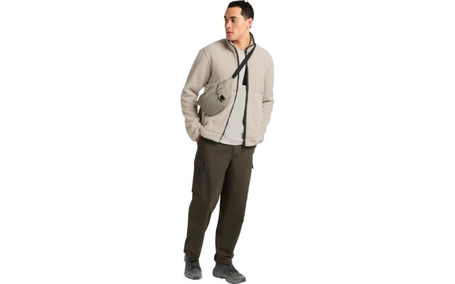 Mann in beige Fleecejacke, hellem Shirt, olivgrünen Cargohosen, grauen Sneakern und olivfarbener Umhängetasche quer über der Brust; schaut nach rechts
