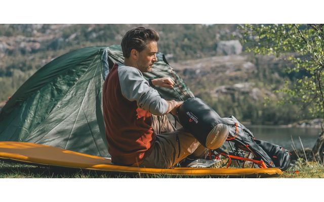 Mann sitzt vor einem Zelt in der Natur und hält ein Fernglas