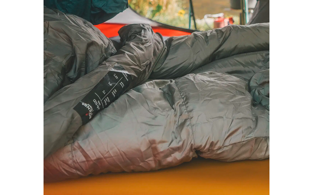 Eine Person mit schwarzer Jacke liegt auf einem orangefarbenen Teppich in einem Zelt