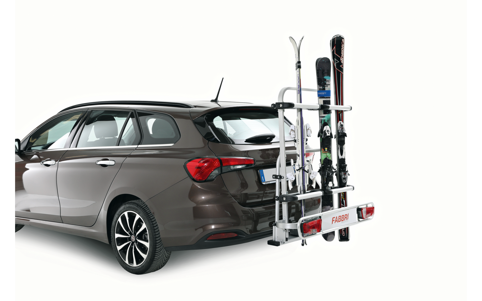 Station wagon marrone vista da dietro a sinistra, con un portasci montato sul gancio di traino con più sci e una tavola da snowboard