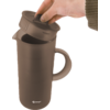 Main avec une manche brune soulève le couvercle amovible d'une tasse brun foncé avec anse ; logo blanc 'Berger' en bas