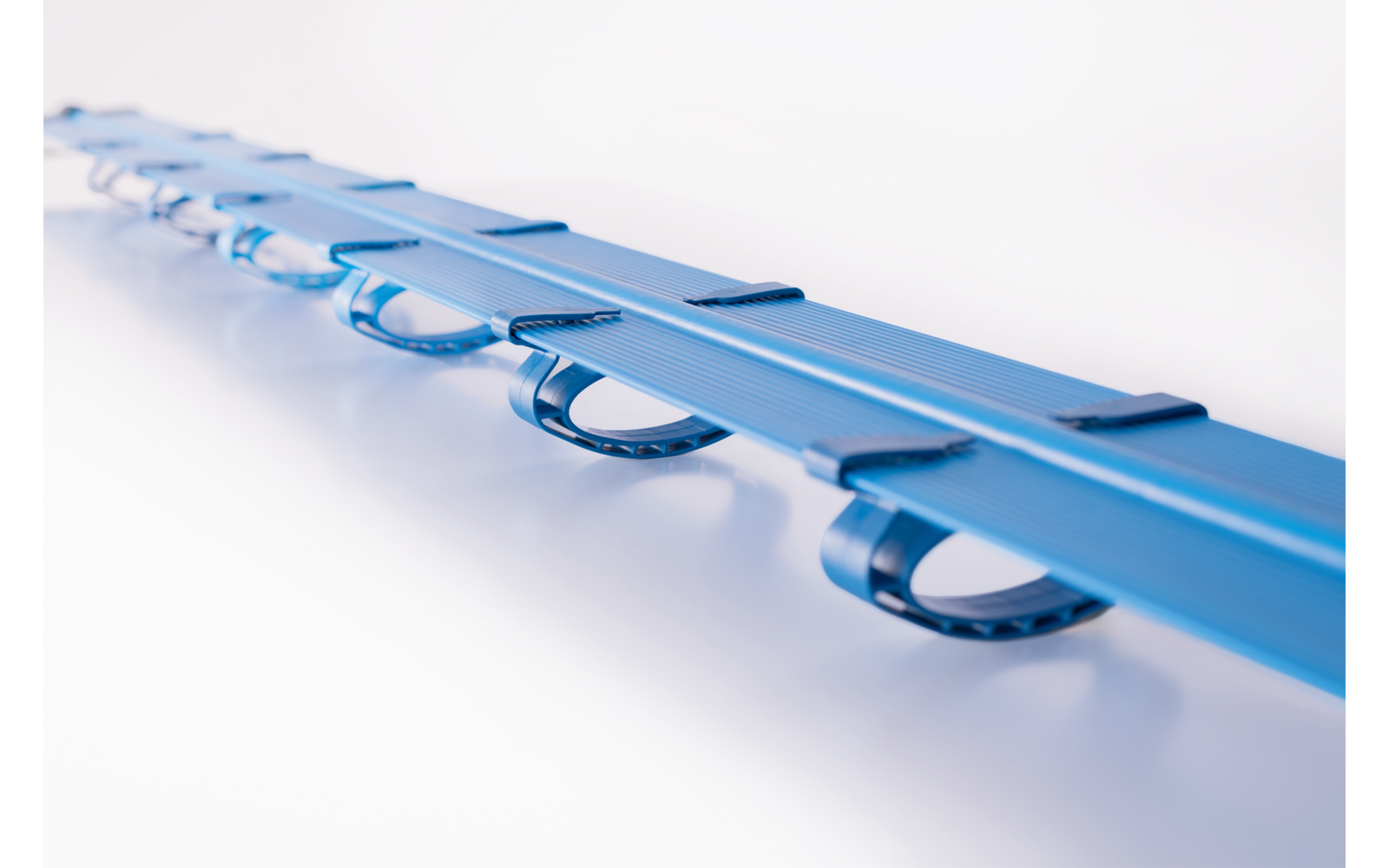 Blaue Kunststoffschiene mit mehreren halbkreisförmigen Schlaufen, auf weißem Hintergrund, perspektivische Nahaufnahme