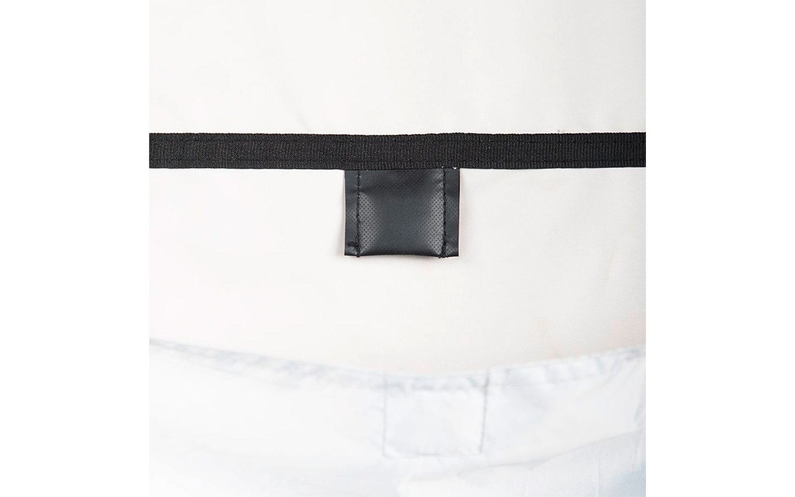 Schwarzes horizontales Band mit mittig platzierter schwarzer rechteckiger Lasche vor weißem Hintergrund; unten hellblauer gesteppter Stoff mit Nähten sichtbar