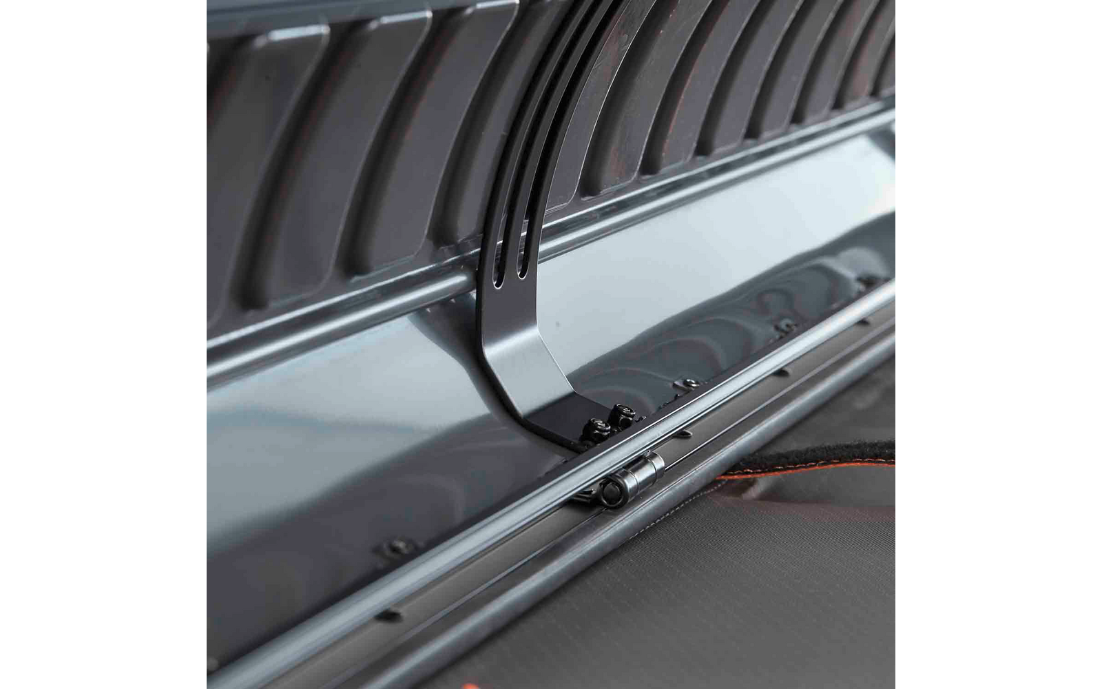 Nahaufnahme eines Metallbügels in einer grauen Kunststoffwanne mit schwarzen Kunststoffrippen, sichtbaren Schrauben und einem schwarzen Gurt mit orangefarbenem Rand