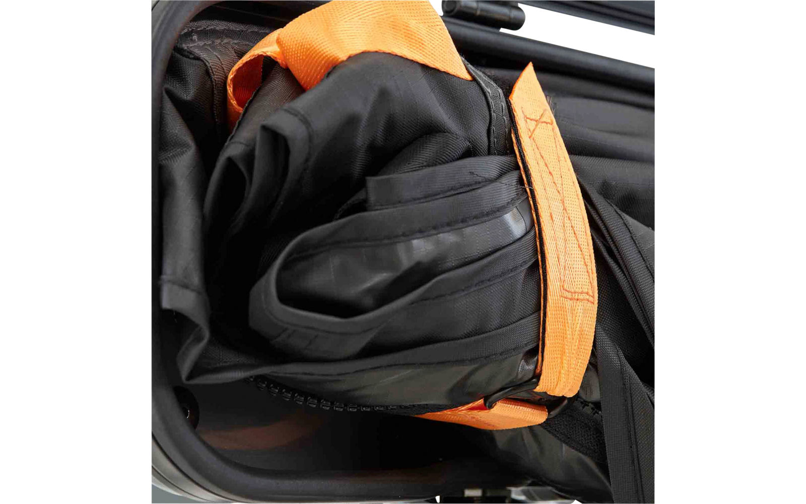 Gefaltetes schwarzes, gummiartiges Material mit sichtbaren Nähten und einem orangefarbenen Gurt, teilweise im silbernen Rahmen einer Kofferöffnung