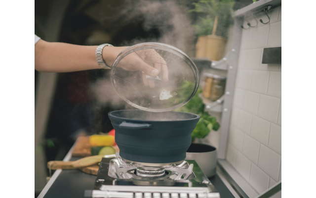 Hand tilt een transparante deksel van een stoofpan af boven een dampende pan in een keuken