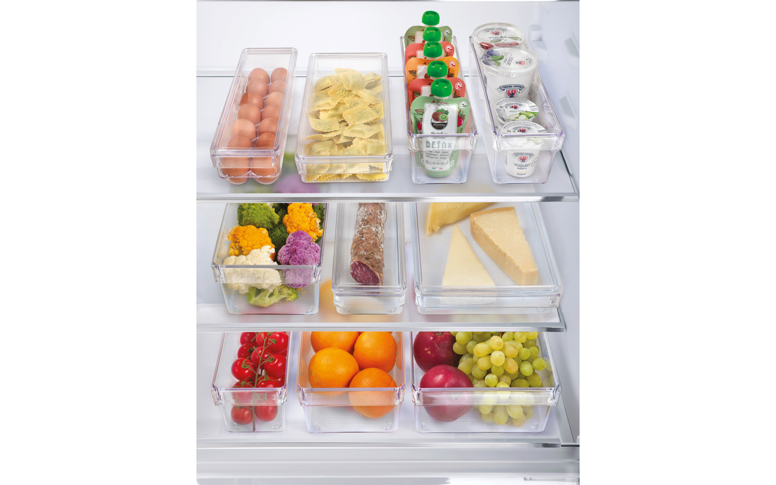Drei transparente Behälter mit unterschiedlichen Lebensmitteln, darunter Wurst, Käse, Obst und Gemüse, auf einem Holztisch