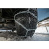 Primer plano de un neumático de coche con cadenas para nieve en una carretera nevada