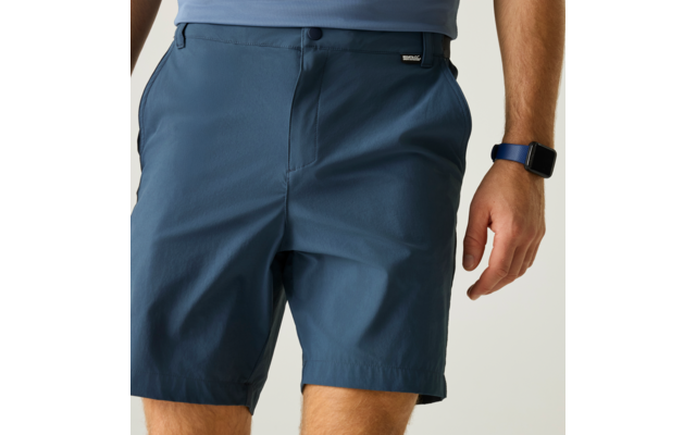Unterer Torso einer Person: blaue Shorts mit Gürtelschlaufen und kleiner schwarzer Etikette, hellblauer Oberteilsaum, sichtbare Oberschenkel und ein Arm mit blauem Smartwatch