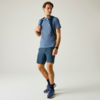 Ein Mann steht, trägt blaues T-Shirt, dunkelblaue Shorts, Rucksack mit Brustgurt, Sportschuhe und Smartwatch