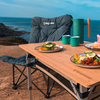 Ein Campingstuhl neben einem Holztisch mit zwei Tellern Essen und zwei Tassen am Meer