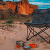 Faltstuhl auf Sand mit Campingkocher und Topf, roter Felsen im Hintergrund
