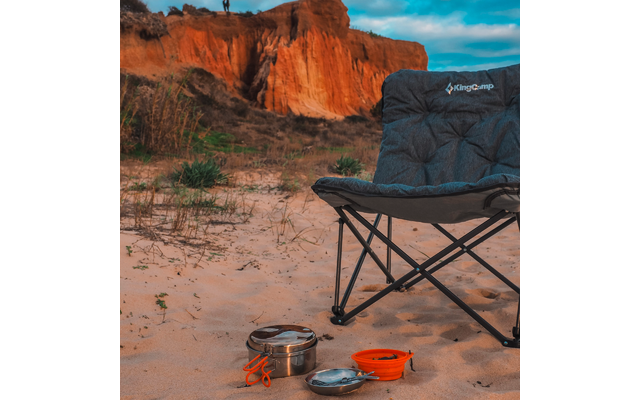 Faltstuhl auf Sand mit Campingkocher und Topf, roter Felsen im Hintergrund