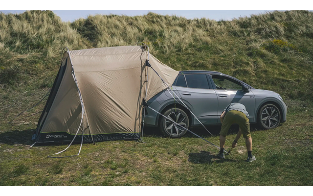 Auto mit Zelt neben einer grünen Wiese und Bäumen im Hintergrund