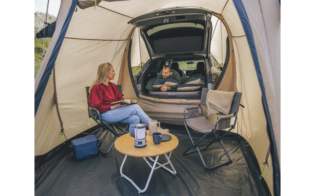 Person sitzt in einem Zelt vor einem kleinen runden Tisch mit Tee und einem Buch