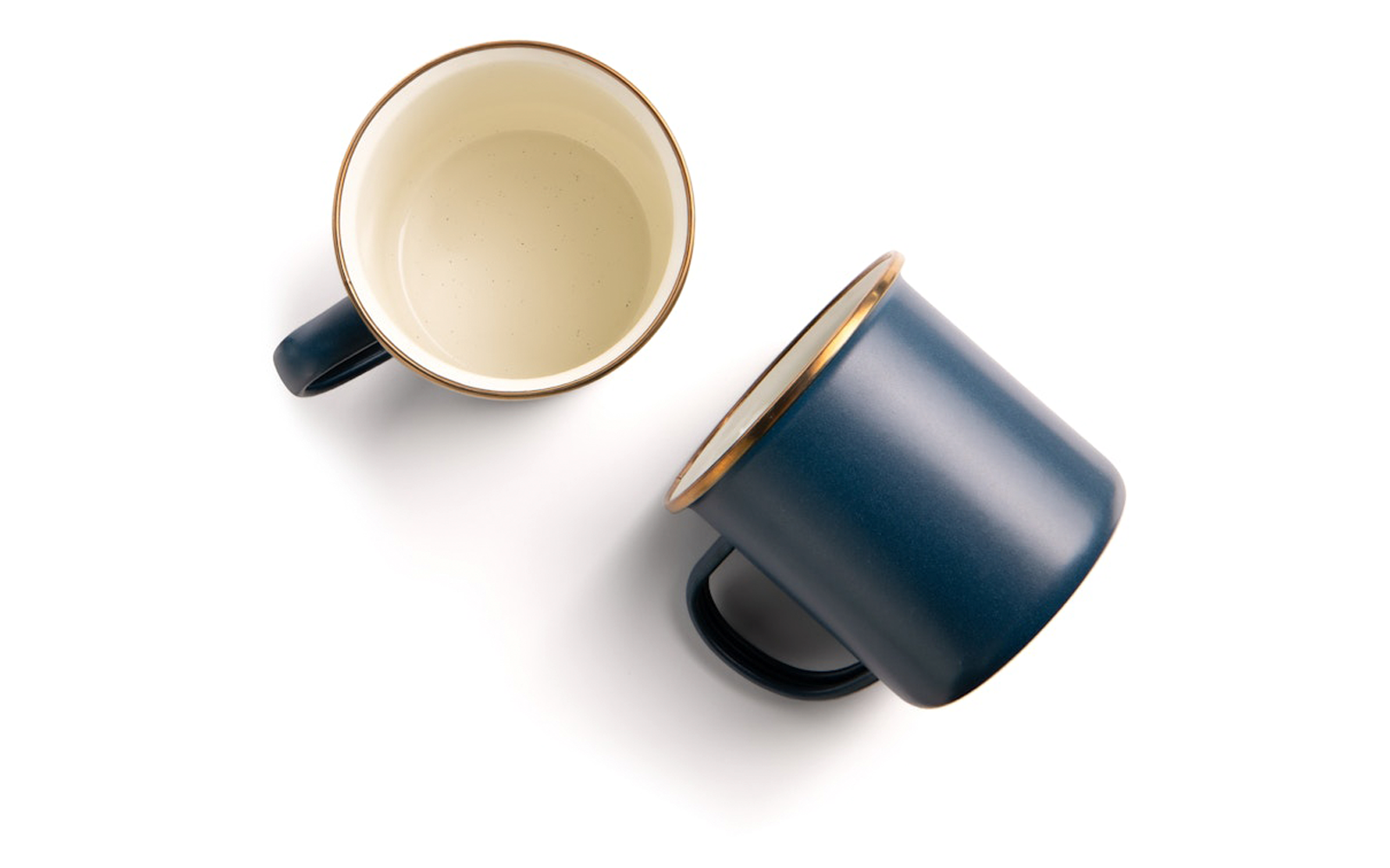 Twee bekers op witte achtergrond: één rechtop met beige binnenzijde en gouden rand, één liggend met donkerblauwe buitenzijde, gouden rand en handvat
