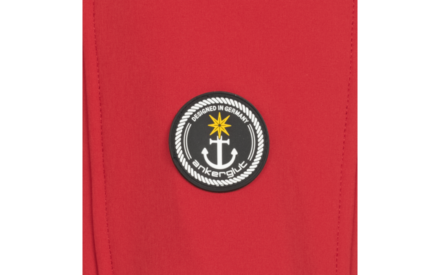 Roter Stoff mit rundem schwarzem Aufnäher. Aufnäher zeigt einen weißen Anker, einen gelben Stern oben, eine weiße Seilrand‑Umrandung und weiße Schrift DESIGNED IN GERMANY sowie ankerglut