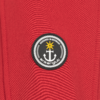 Roter Stoff mit rundem schwarzem Aufnäher. Aufnäher zeigt einen weißen Anker, einen gelben Stern oben, eine weiße Seilrand‑Umrandung und weiße Schrift DESIGNED IN GERMANY sowie ankerglut