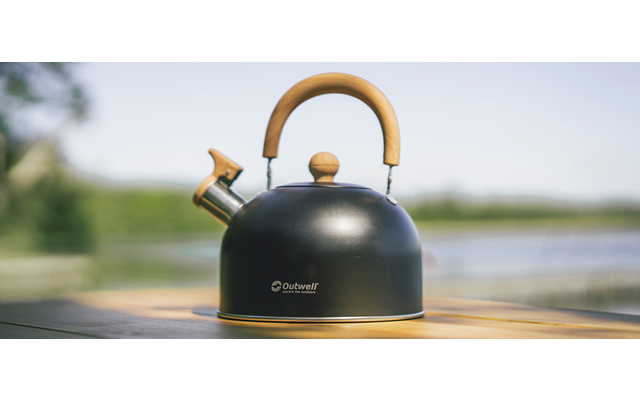 Zwarte theeketel met houten handvat op houten oppervlakte, wazige achtergrond met lucht en water