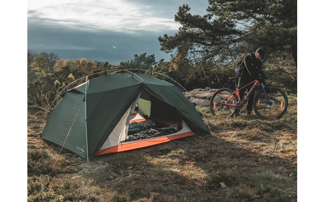 Ein grünes Zelt steht auf einer Wiese neben einem Fahrrad unter Bäumen