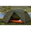 Green dome tent with open front flap showing orange-and-white interior, pitched on grass by a body of water with trees and hills in the background; tent poles and guy lines visible