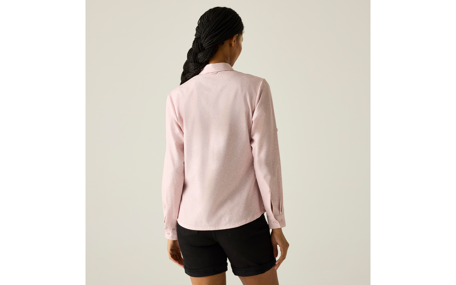 Person von hinten, rosa langärmliges Hemd, schwarze Shorts, geflochtenes Haar, heller beiger Hintergrund