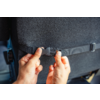 Two hands fasten a black plastic buckle on a strap attached to the back of a car seat