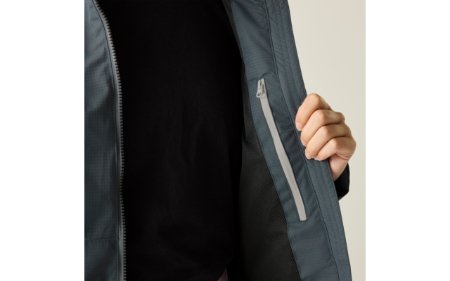 Person mit schwarzem T-Shirt hält offene graue Jacke, Innenseite mit senkrechter Reißverschlusstasche sichtbar, heller Hintergrund