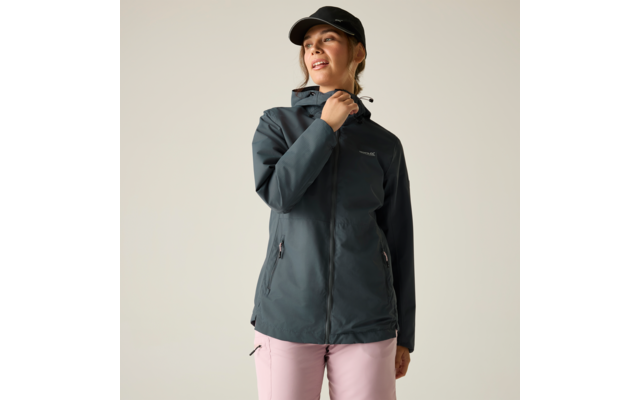 Person vor hellem Hintergrund trägt dunkelgraue Kapuzenjacke, schwarze Baseballkappe und hellrosa Hose; rechte Hand hält den Jackenkragen, Blick nach oben rechts