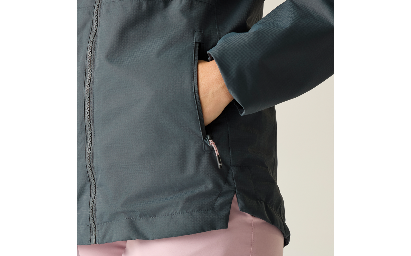 Oberkörper einer Person mit dunkelgrüner Jacke, rechte Hand in seitlicher Reißverschlusstasche, rosa Hose