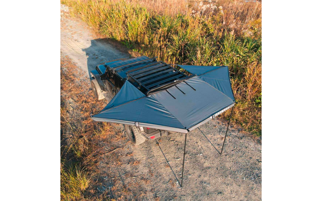 Draufsicht auf ein Fahrzeug mit montiertem Dachgepäckträger und ausgefahrener Markise, die von vier Stützen gehalten wird; Kiesweg und hohes Gras daneben