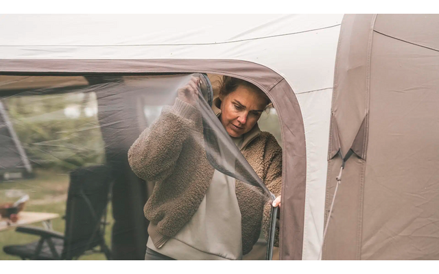 Mann mit Brille steht vor einem Zelt und öffnet den Reißverschluss