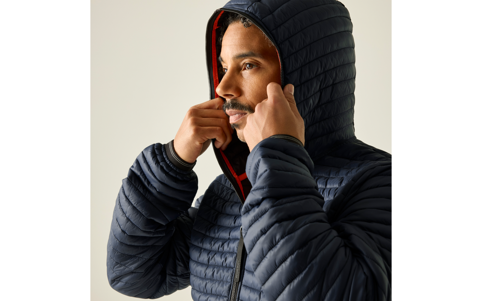 Person zieht die Kapuze einer dunkelblauen, gesteppte Jacke mit rotem Futter über den Kopf, Seitenprofil sichtbar